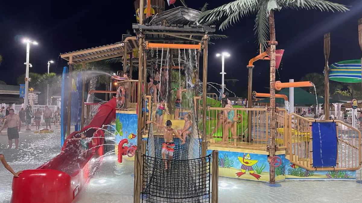 Featuring a vibrant water park scene with a colorful water slide, children playing, and playful water features, this image conveys the fun and lively energy of the resort’s water amenities. The scene is full of action, laughter, and family enjoyment—perfect for illustrating the seasonal excitement of the splash pad and outdoor park.