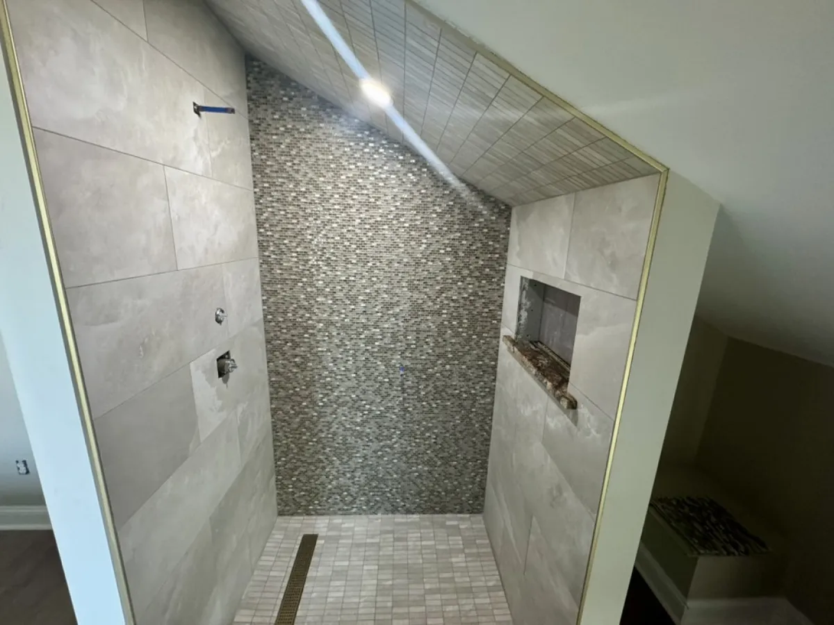This image shows a stylish bathroom interior with a textured stone wall, modern shower fixtures, and warm recessed lighting. Though not a kitchen or dining area, the space exudes an upscale, luxury feel with high-end finishes.