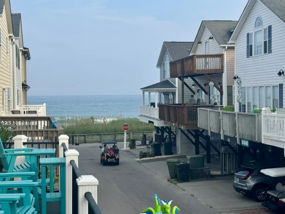 A scenic coastal view featuring a stretch of beach, nearby houses, a vehicle traveling along the road, and a stop sign. The image evokes a sense of accessibility and proximity to the beach, suggesting the ease of exploring local attractions and enjoying outdoor activities with family or friends.