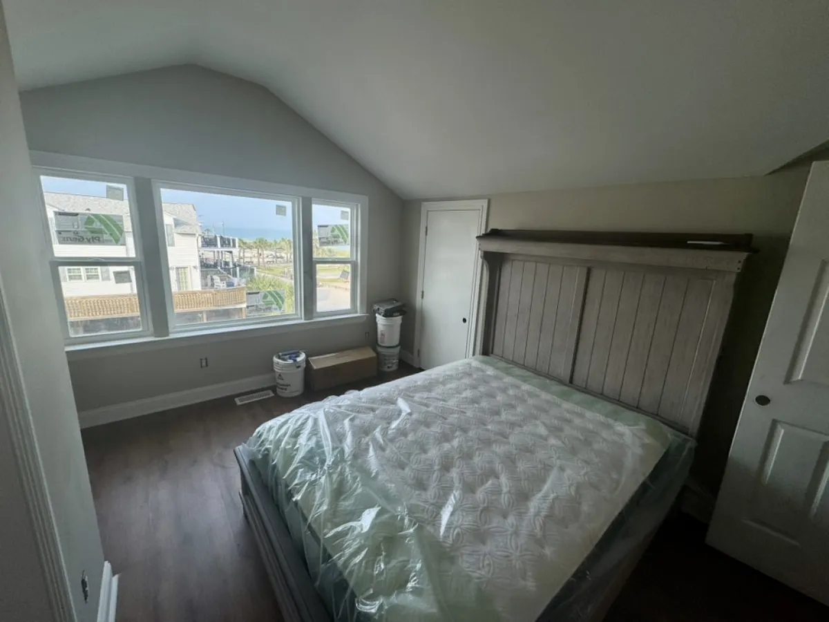 A tranquil bedroom setting with a neatly made bed, large windows allowing in natural light, and simple, elegant cabinetry. The room exudes comfort and an inviting atmosphere.