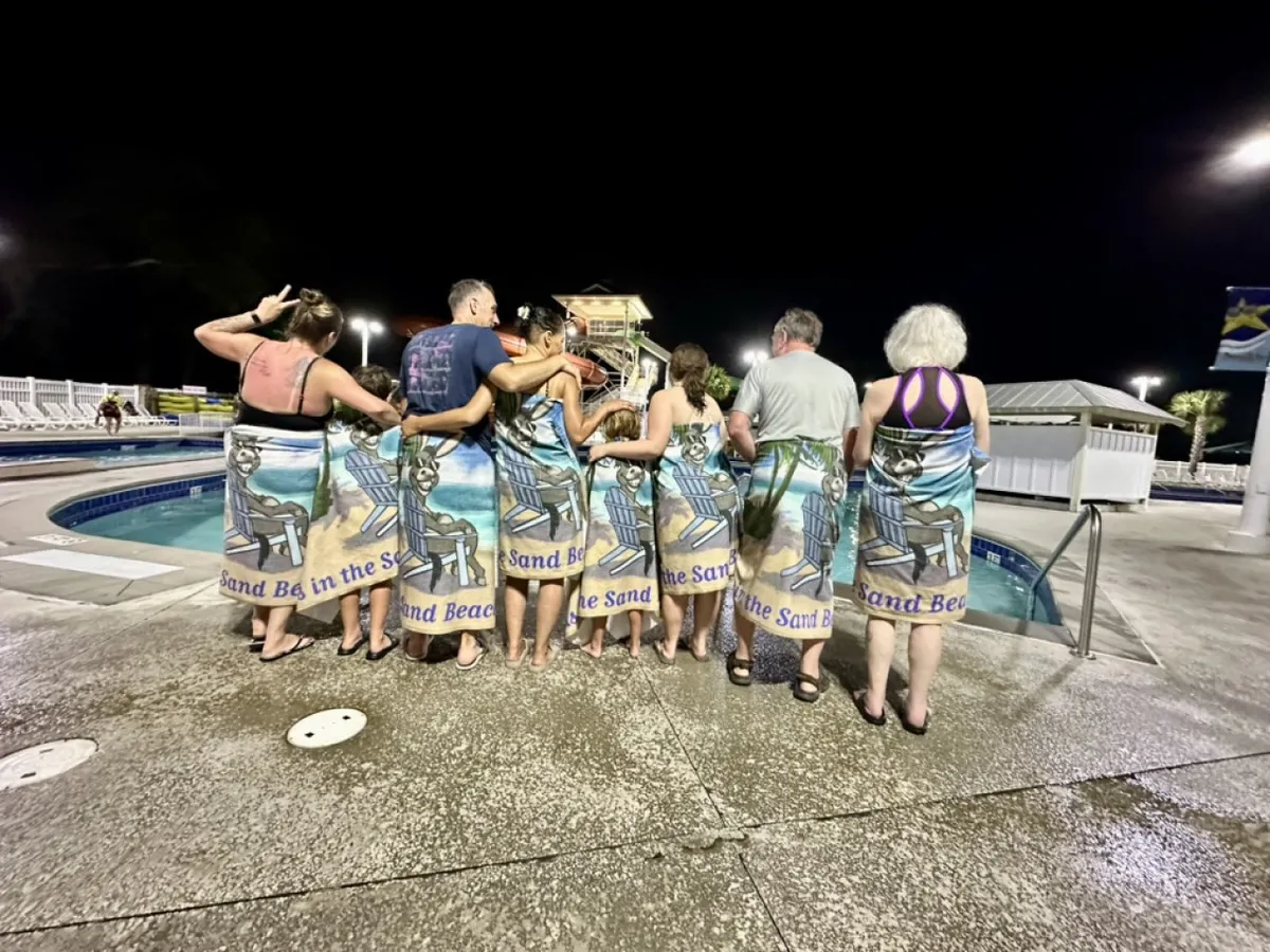 An inviting nighttime pool scene, with a group of people relaxing in towels by the illuminated swimming pool, radiates warmth, relaxation, and camaraderie. The lighting and atmosphere suggest year-round enjoyment and relaxation with friends and family, especially in the evenings or cooler weather.