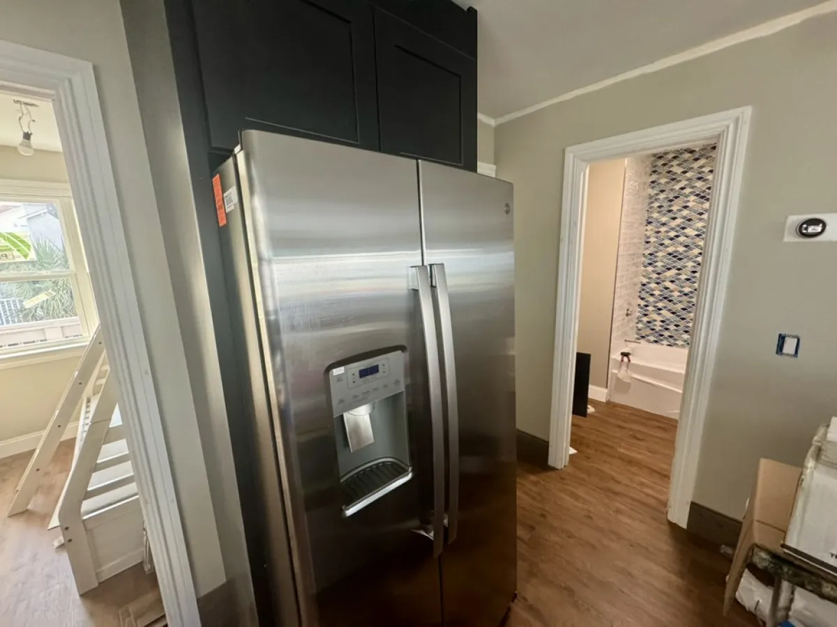 A view of the kitchen area featuring a stainless steel refrigerator, dark cabinetry, and a doorway leading to the bathroom. The space is modern and functional, suggesting an open flow into living and dining spaces.