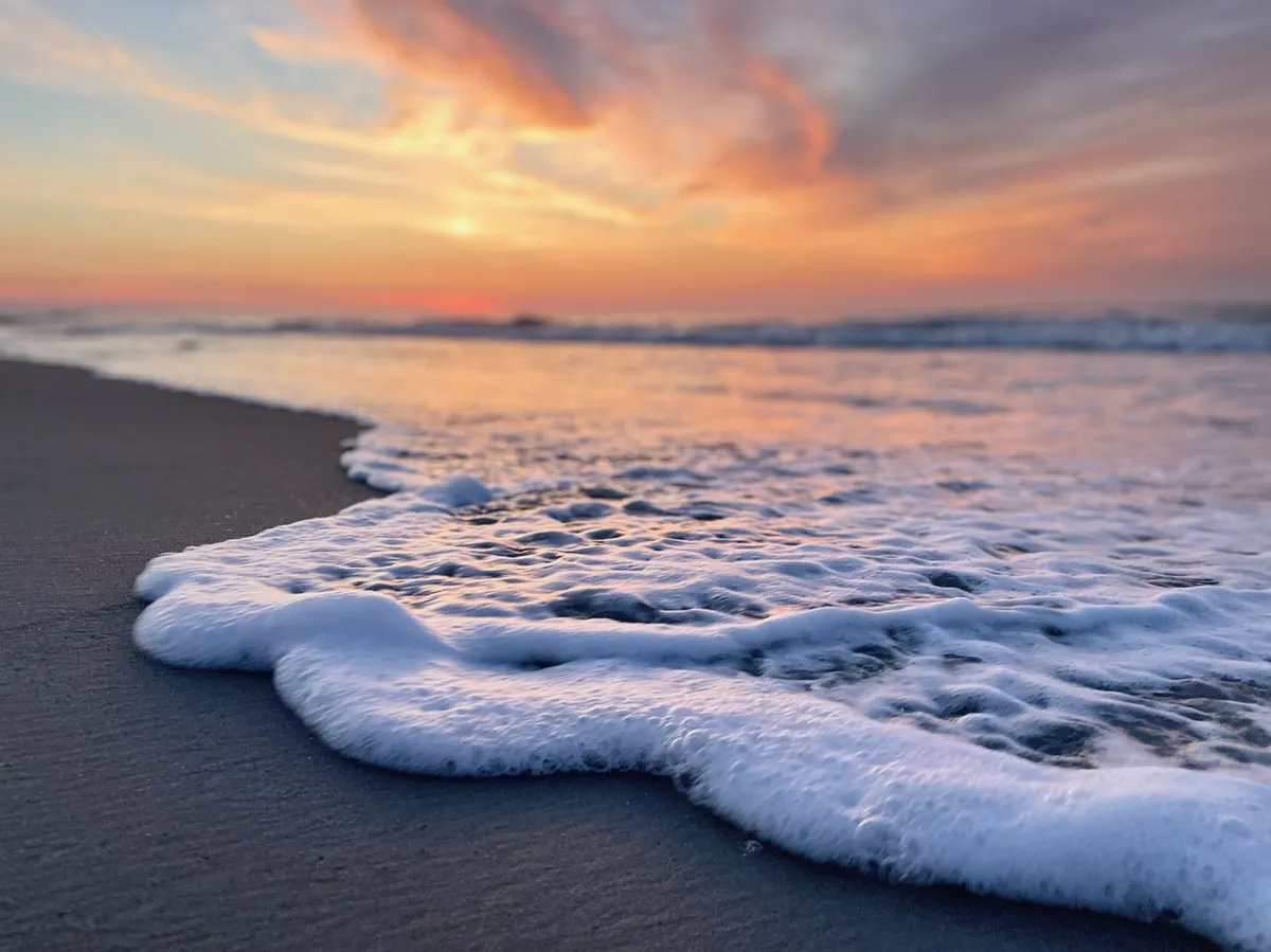 A serene beachscape with gentle waves, a colorful sky, and sandy shore, perfect for beachcombing, sunset watching, and capturing memorable photos. The ambiance is calm yet inviting, ideal for Instagram-worthy moments.